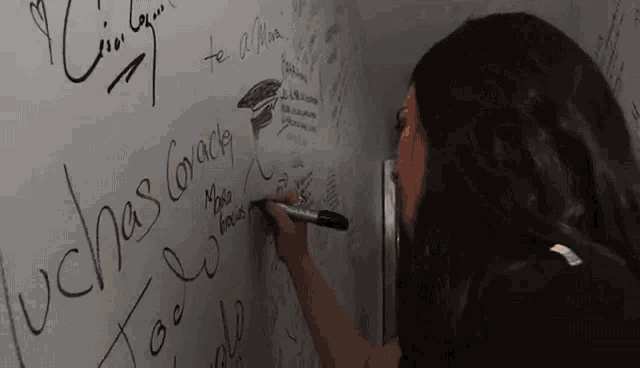a woman writes on a white board with a marker that says " ochas corazón "