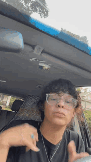 a woman wearing glasses and a necklace is sitting in a car .