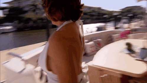 a woman in a white tank top is walking on a boat
