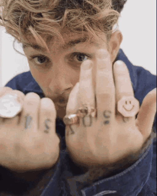 a man with a smiley face ring on his finger has a tattoo of the letter s on his finger