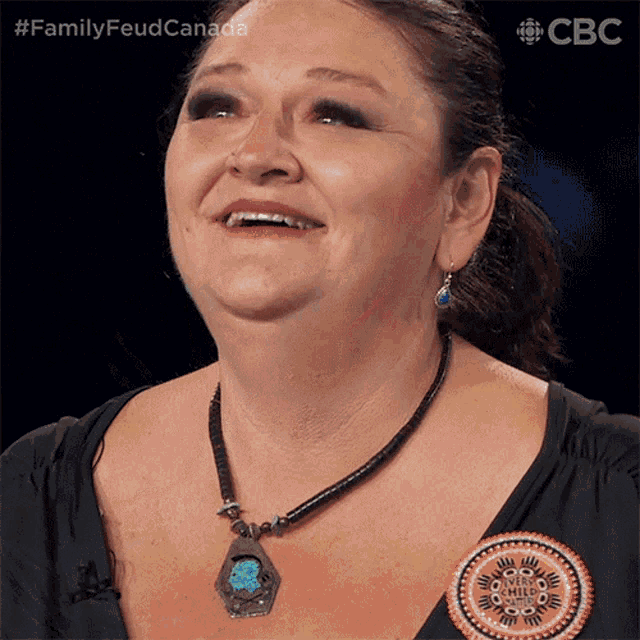 a woman wearing a necklace with a turquoise pendant is smiling for a family feud canada ad