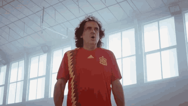 a man wearing a red adidas jersey stands in front of a window