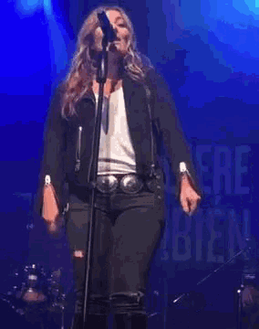 a woman in a black jacket is singing into a microphone on stage