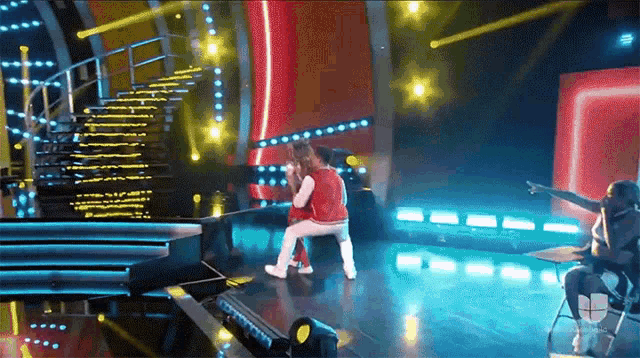a group of people dancing on a stage with a woman pointing