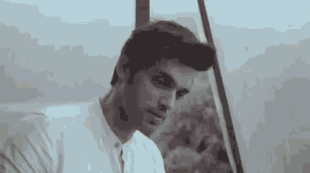 a man in a white shirt is sitting in front of a window and looking out .