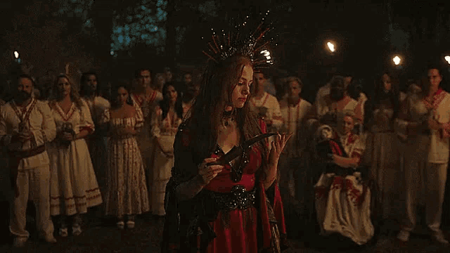 a woman in a red dress is holding a sword in front of a crowd of people