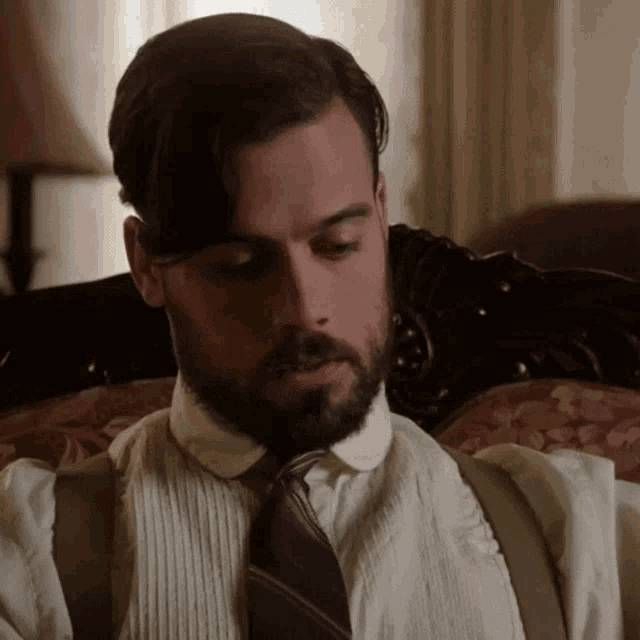 a man with a beard and suspenders is sitting on a chair