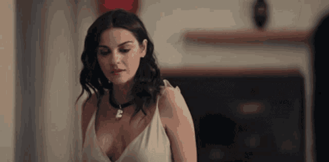 a woman in a white dress and choker is standing in front of a fireplace in a living room .
