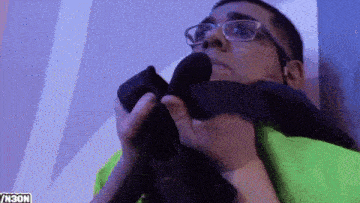 a man wearing glasses and a green shirt is holding a black object with the letters n30n on the bottom right