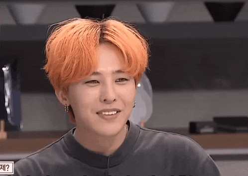 a young man with orange hair is smiling and wearing a black sweater