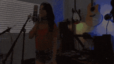 a woman sings into a microphone in a room with guitars hanging on the wall