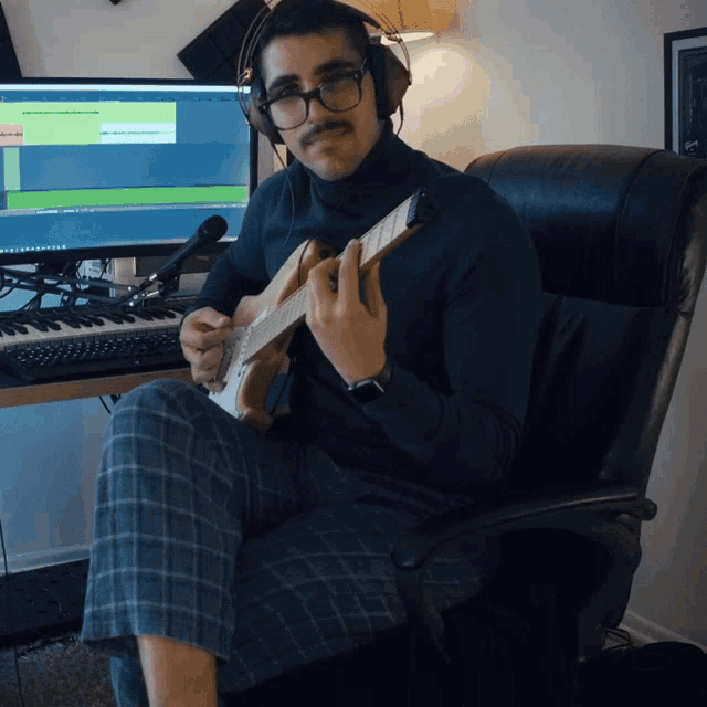 a man wearing headphones playing a guitar in front of a computer monitor