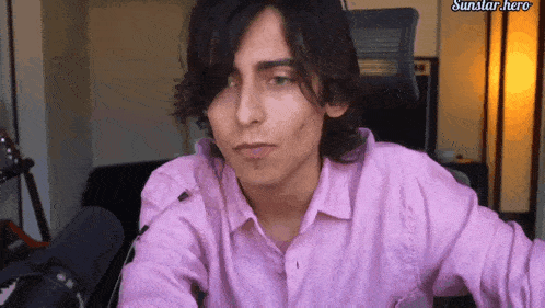 a man in a pink shirt is sitting in front of a microphone with the words sunstar hero on the bottom right