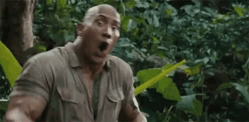 a man is sitting in the jungle with his mouth open and a surprised look on his face .