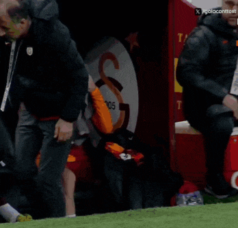 a man in a sixt shirt sits on a bench on a soccer field