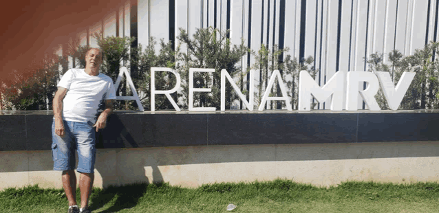 a man stands in front of a sign that reads arenamrv