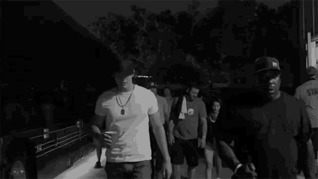 a black and white photo of a group of men walking down a street at night .