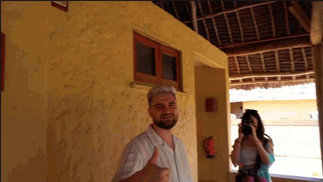 a man is giving a thumbs up while a woman takes a picture