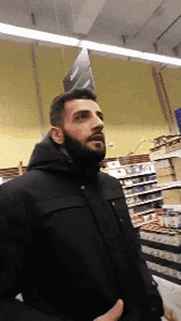 a man with a beard and a black jacket is standing in a store