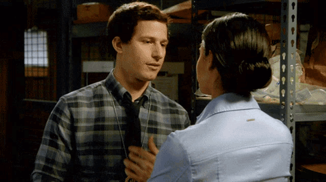 a man in a plaid shirt and tie talks to a woman