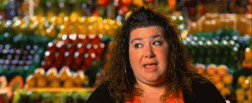 a woman making a funny face in front of a fruit stand .