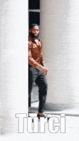 a man in a brown shirt and black pants is standing behind a white pillar and the word turci is on the bottom
