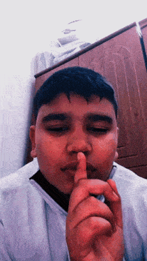 a young boy holds his finger to his mouth in a silence gesture