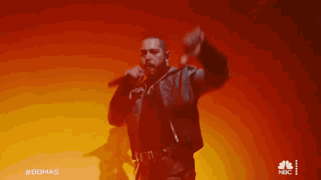 a man is singing into a microphone on a stage with a red background .
