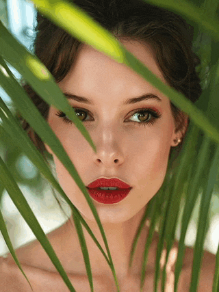 a woman with red lips is behind a palm tree