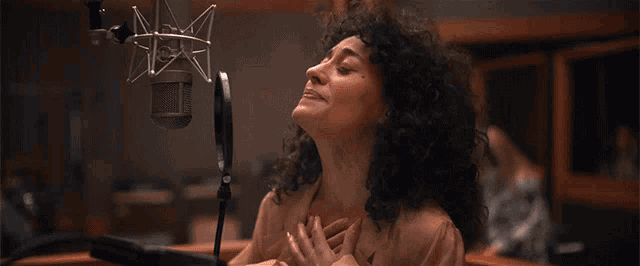 a woman with curly hair stands in front of a microphone