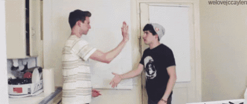 two men are standing next to each other in a kitchen and one of them is wearing a beanie .