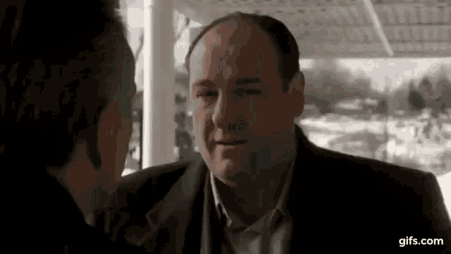 a man in a suit is talking to another man in a suit on a porch .