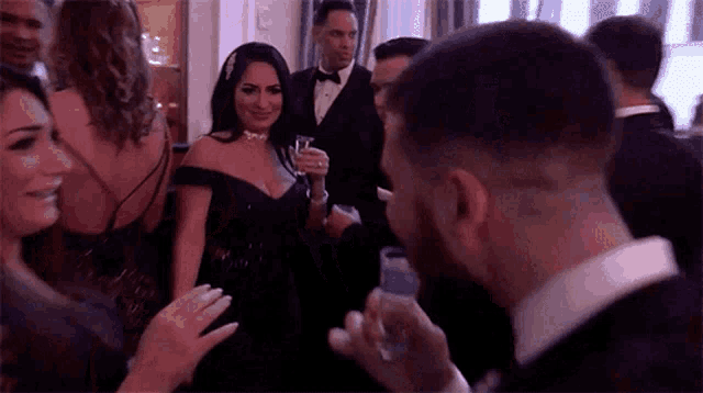 a man in a tuxedo is holding a glass of wine while standing in a crowd of people .