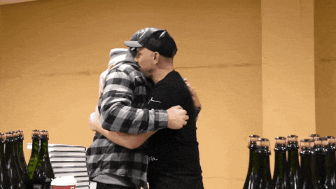 two men hugging each other in front of a wall of bottles