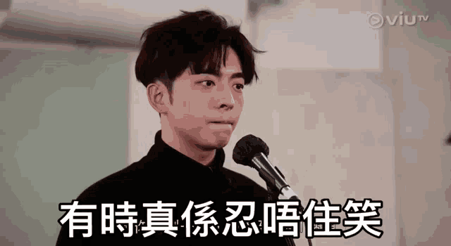 a man in a black shirt is standing in front of a microphone with chinese writing on it .