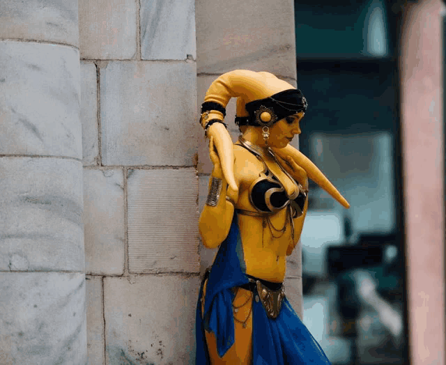 a woman in a yellow and blue costume is leaning against a stone wall