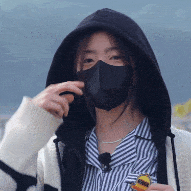 a woman wearing a black mask and a white sweater holds a badge that says ' i love you '