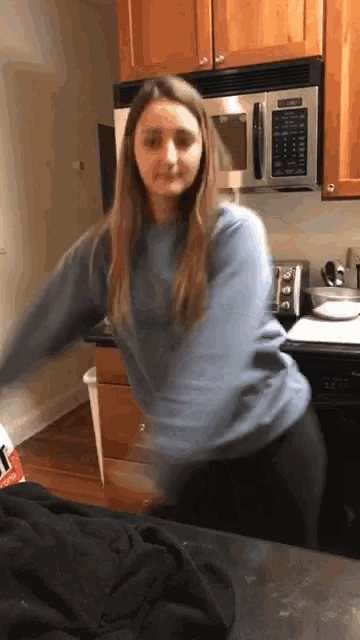 a woman in a blue sweater is standing in a kitchen near a microwave