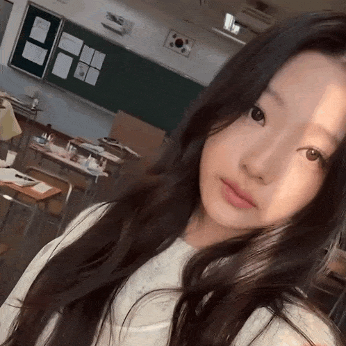 a young girl taking a selfie in a classroom with a korean flag on the wall