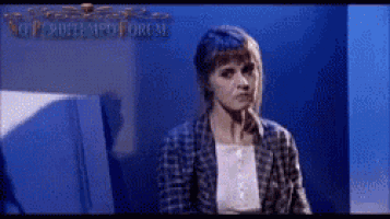 a woman in a plaid shirt is sitting in front of a blue wall with the word forum on it .