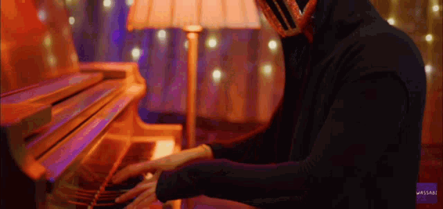 a man in a black hoodie plays a piano in front of a lamp