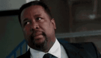 a man in a suit and tie is sitting with his eyes closed and his mouth open .