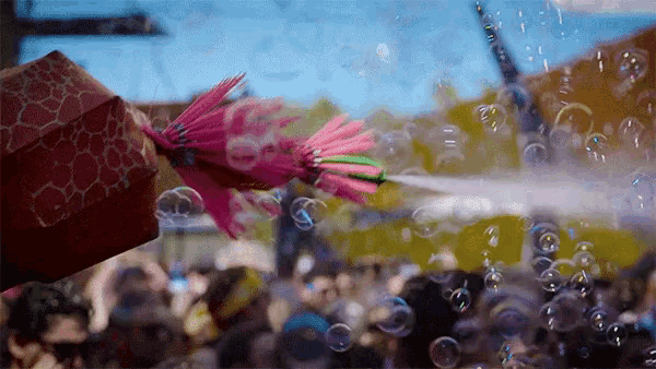 a person is holding an umbrella in front of a crowd of people while a pink flower is being sprayed with bubbles