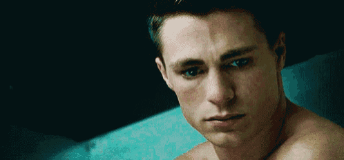 a shirtless young man is sitting on a blue couch looking at the camera .