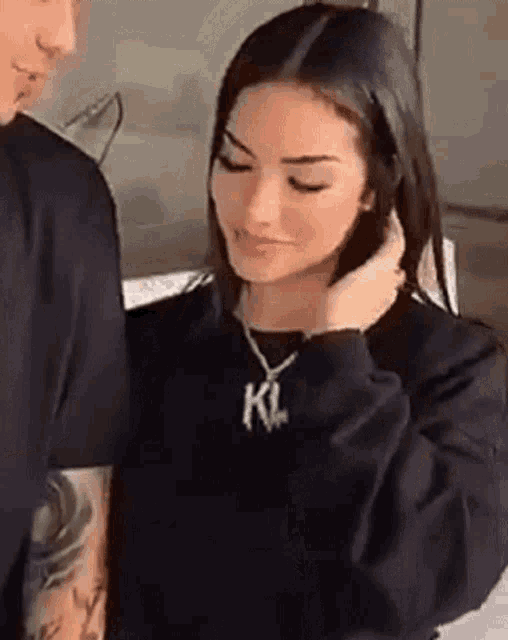 a man and a woman are standing next to each other and the woman is wearing a necklace with a letter k on it .