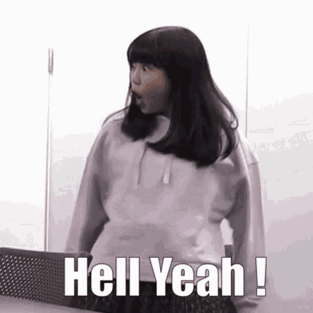 a girl in a purple sweatshirt is standing in front of a wall and saying `` hell yeah ! ''