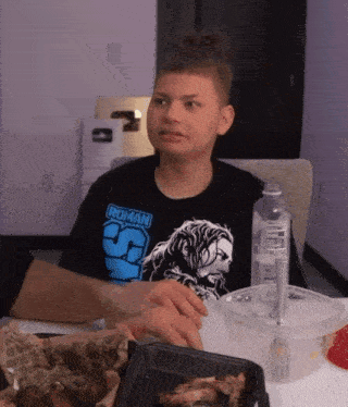 a man wearing a roman t-shirt sits at a table
