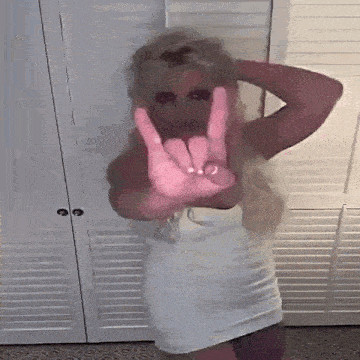 a woman in a white dress is standing in front of a closet and making a peace sign with her hands .