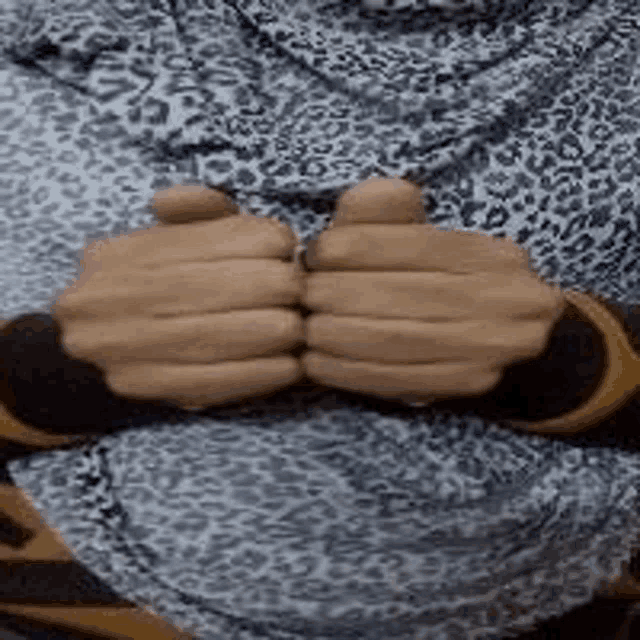 a woman wearing a leopard print hijab is holding her hands together in front of her chest .