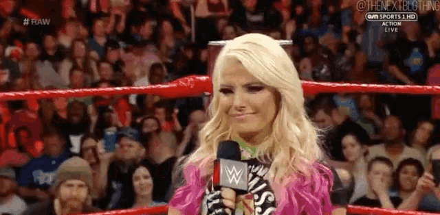 a woman is standing in a wrestling ring holding a microphone in front of a crowd .
